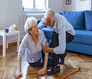 Senior couple in a living room with one person on the floor and the other helping.